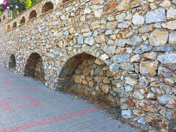 Farklı ebat ve şekillerde doğal taştan yapılmış girinti ler ve kemerler ile duvarın bir parçası. Eski taş bina boyunca yol. Yakın çekim, güzel arka plan ve ilginç doku.