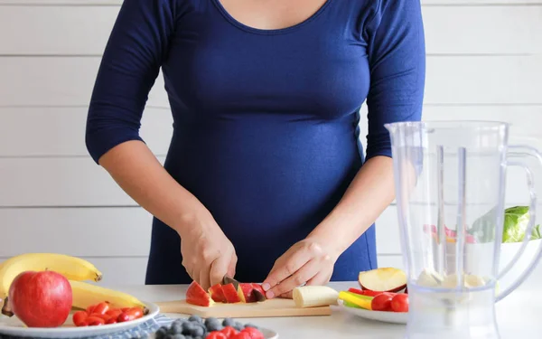 pregnant woman cooking and cutting fruit for fruit blender, healthy
