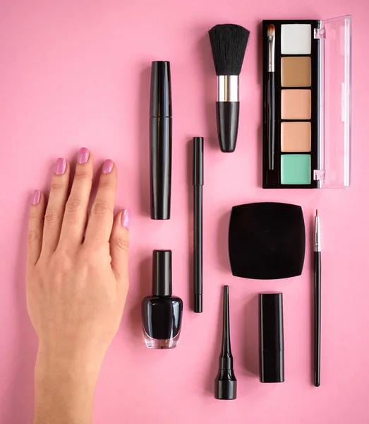 Different makeup products composition with hand on pink background