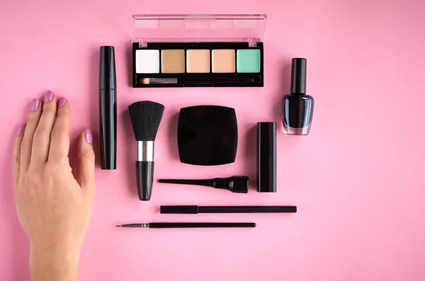 Different makeup products composition with hand on pink background