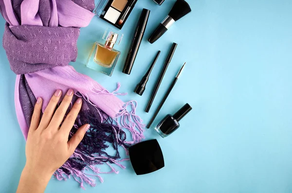 Different makeup products composition with hand on blue background