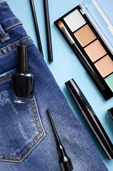 Different makeup products composition with jeans on blue background