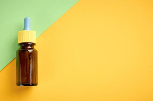 Burun damlaşişe kompozisyon, sarı ve yeşil arka plan üzerinde cam şişe — Stok fotoğraf
