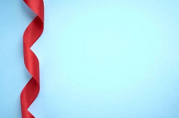 Red ribbon on blue background composition, flat lay
