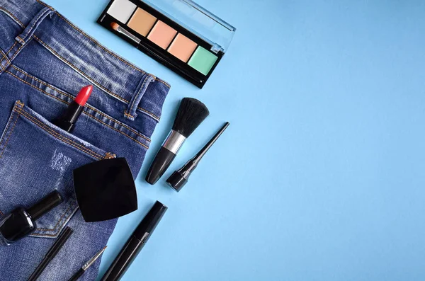 Different makeup products composition with jeans on blue background
