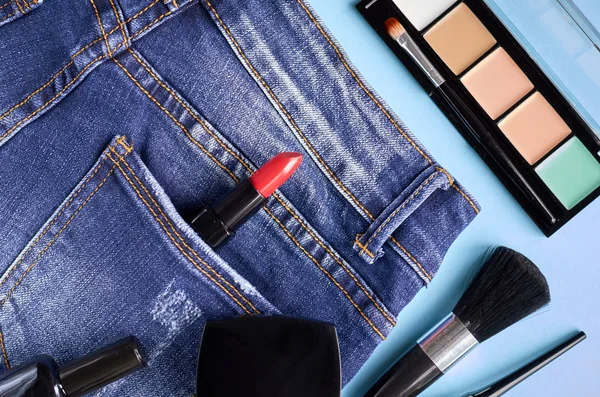 Different makeup products composition with jeans on blue background