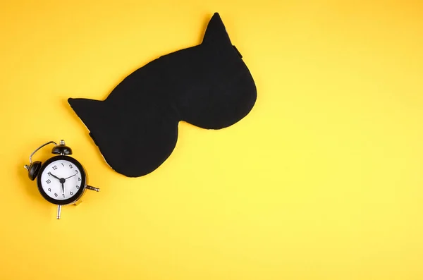 黄色の背景構成に時計付きの黒い睡眠マスク、耳付き猫マスク — ストック写真