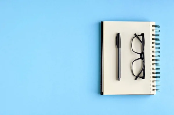 Cuaderno negro de gafas, bolígrafo y papel sobre fondo azul composición . — Foto de Stock
