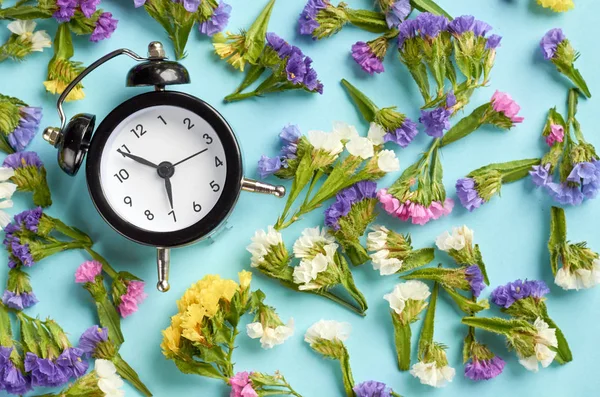 Relógio despertador com flores coloridas na composição de fundo azul . — Fotografia de Stock