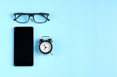 Siyah gözlük, çalar saat ve cep telefonu mavi arka plan kompozisyon.