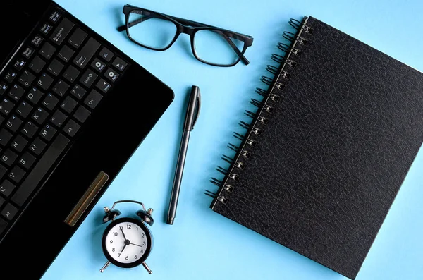 Gafas negras, despertador y teclado portátil sobre fondo azul . — Foto de Stock