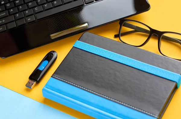 Gafas negras, portátil, flash USB y teclado portátil en azul y amarillo composición de fondo . — Foto de Stock