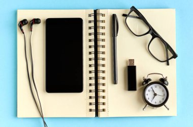 Siyah gözlük, cep telefonu, kağıt not defteri, çalar saat ve mavi arka plan kompozisyon kulaklık.