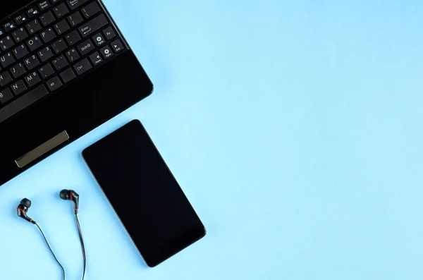 Teclado portátil negro, teléfono celular y auriculares en la composición de fondo azul . — Foto de Stock