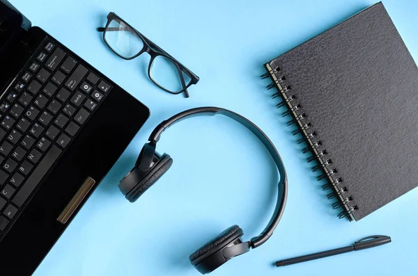 Gafas negras, auriculares, portátil y teclado portátil en composición de fondo azul . — Foto de Stock