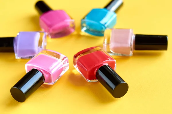 Color nail polish bottles on yellow background composition.