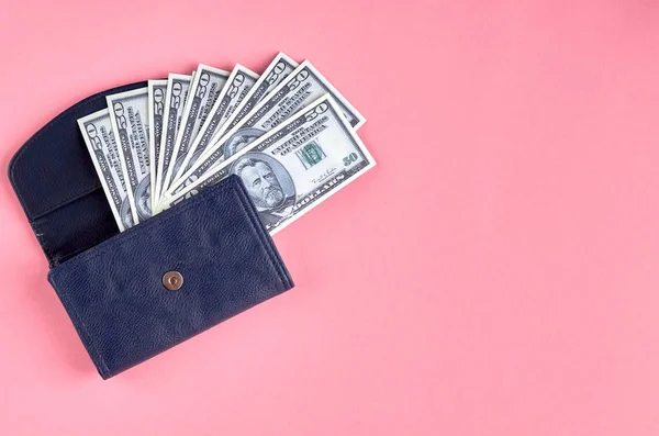 Dark blue leather wallet with money on pink background composition.