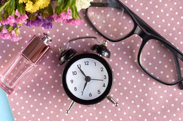 Alarm clock, black glasses and perfume bottle on napkin background composition.