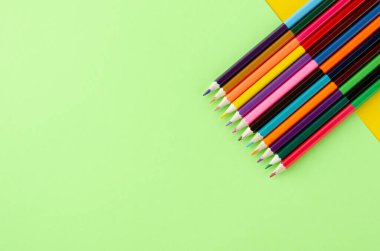 Sarı ve yeşil arkaplanda renkli kalemler kompozisyonu.