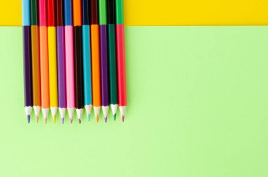 Sarı ve yeşil arkaplanda renkli kalemler kompozisyonu.