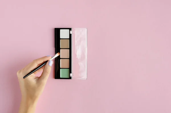 Mano con maquillaje sombras composición de la paleta sobre fondo rosa . — Foto de Stock