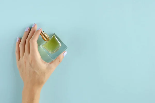 Hand met parfumflessamenstelling op blauwe achtergrond. — Stockfoto