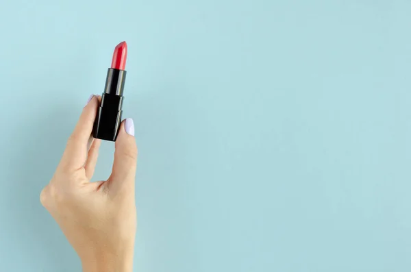 Mano con composición de lápiz labial rojo sobre fondo azul . — Foto de Stock