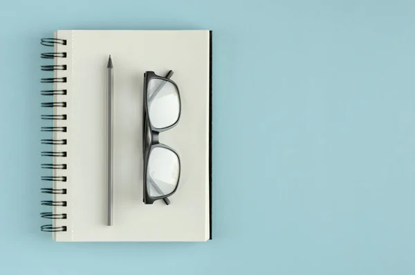 Bloc de notas con anteojos y composición de lápiz sobre fondo azul . — Foto de Stock