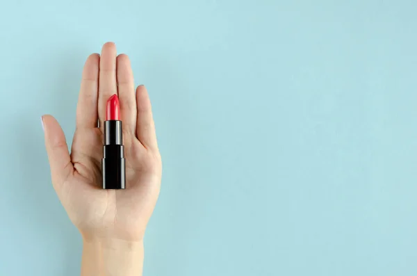 Mano con composición de lápiz labial rojo sobre fondo azul . — Foto de Stock