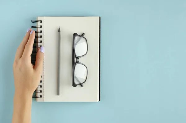 손으로 노트 패드, 안경 및 파란 배경에 연필 구성을 가지고. — 스톡 사진
