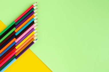 Sarı ve yeşil arkaplanda renkli kalemler kompozisyonu.