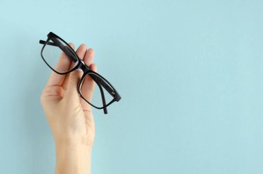 Mavi arkaplanda gözlük bileşimi olan el..