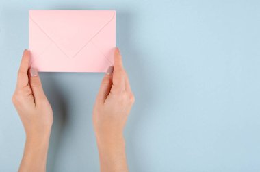 Mavi arka planda pembe kağıt zarf bileşimi olan el..