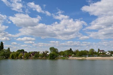 Göl kıyısındaki küçük köy, yeşil ağaçlar ve mavi gökyüzünde kabarık bulutlar..