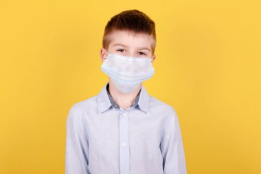 Tıbbi maskeli esmer bir çocuğun portresi. Sarı arkaplanda izole edilmiş.
