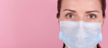 Tıbbi maskeli esmer bir kızın portresi. Pembe arka planda izole edilmiş, afiş.