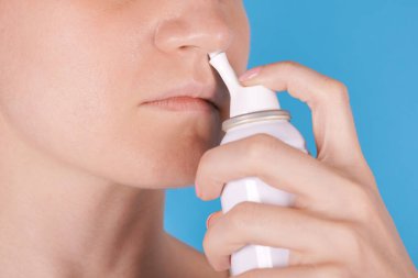 Burun spreyi kullanan bir kız. Mavi arkaplanda izole.