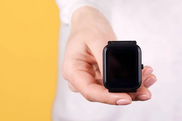 Black smart watch in hand on yellow background. Close up photo.