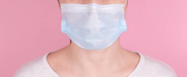 Tıbbi maskeli esmer bir kızın portresi. Pembe arka planda izole edilmiş, afiş.