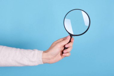 Magnifying glass in hand on a blue background. clipart