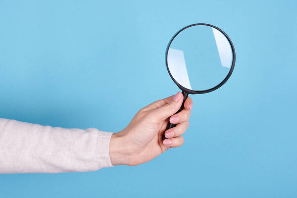 Magnifying glass in hand on a blue background.