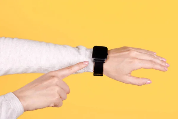 Black smart watch on hand on yellow background. Finger pointing on object.