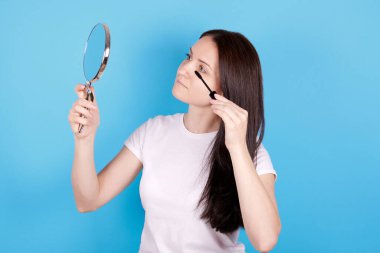 Kız aynaya bakıyor ve maskara kullanıyor..