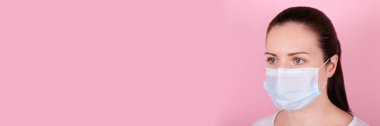 Tıbbi maskeli esmer bir kızın portresi, başka tarafa bakıyor. Pembe arka planda izole edilmiş.