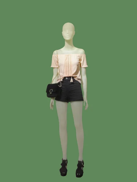 Yeşil arka plan üzerinde siyah şort ve pembe bluz giymiş tam uzunlukta kadın manken.