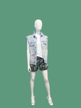 Tam uzunlukta kadın manken yelek denim ceket ve yeşil arka plan üzerinde izole şort giymiş. Hiçbir marka isimleri veya telif hakkı nesneleri.
