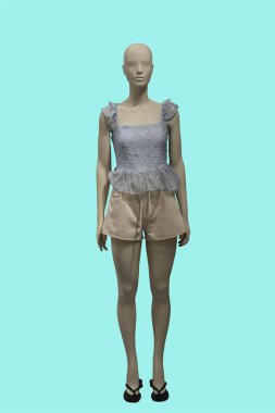 Yeşil arka planda izole edilmiş dantelli ve bej şortlu şık bir bluz giyen bir kadın vitrin mankeni.