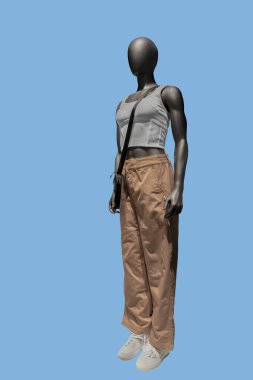 Mavi arka planda beyaz bluz ve bej pantolon giyen bir kadın vitrin mankeni.