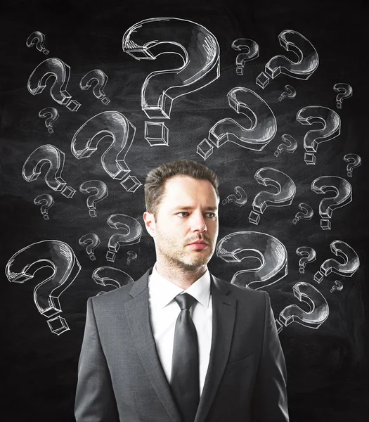 Thooughtful Young Businessman Question Marks Standing Chalkboard Background Confusion Doubt — Stock Photo, Image
