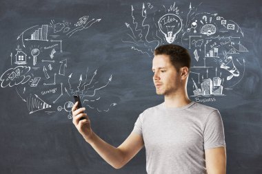 Yan yaratıcı iş kroki kara tahta duvar zemin üzerine smartphone kullanarak çekici genç adam portresi. Teknoloji, iletişim ve ekonomi kavramı 